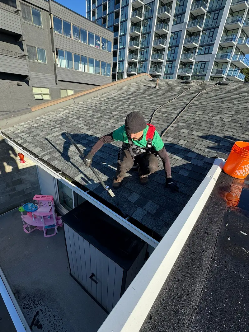 Two Pines technician cleaning gutters on a flat-roof strata building in Victoria BC
